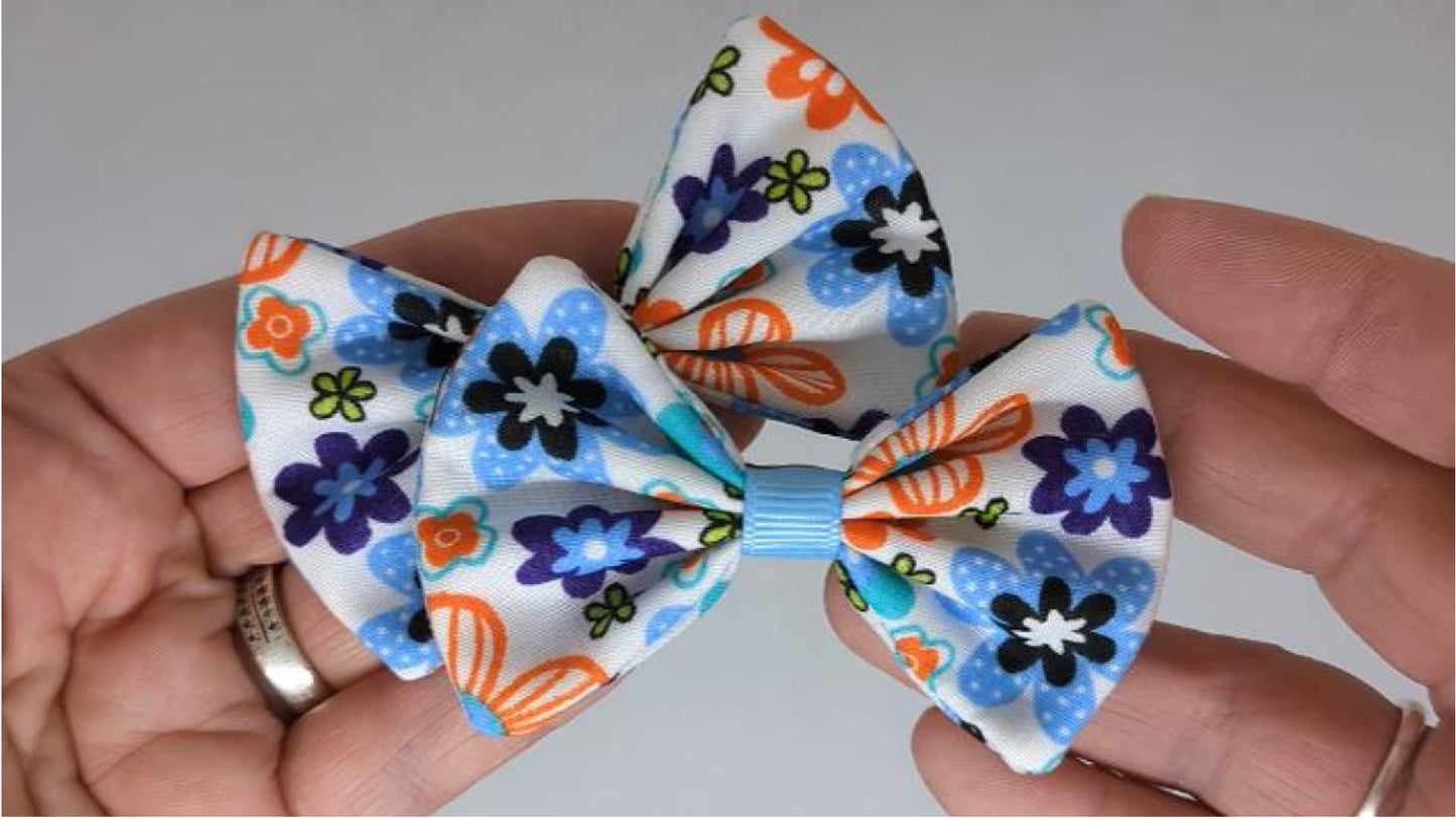 Close-up of funky floral fabric hair bows on alligator clips, measuring 7cm x 5cm, showcasing the vibrant blue, orange, and white floral pattern.