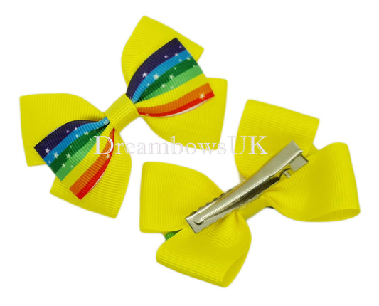 Yellow and rainbow striped hair bows on a flat surface with alligator clips, highlighting the unique one-of-a-kind design and vibrant rainbow stripes.